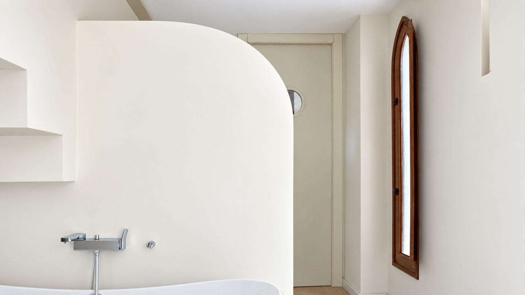 Seamless microcement bathroom walls wrapping a curved bath, with a built-in niche and no grout lines